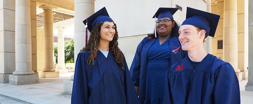 三个美国毕业生戴着帽子，穿着学士服，面带微笑.